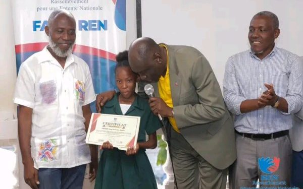 L’ancien ministre Jimmy Albert, le dos penché et un micro à la main, remet un certificat à une récipiendaire.